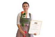 Frau im Dirndl hält Rose in einer und Urkunde in anderer Hand